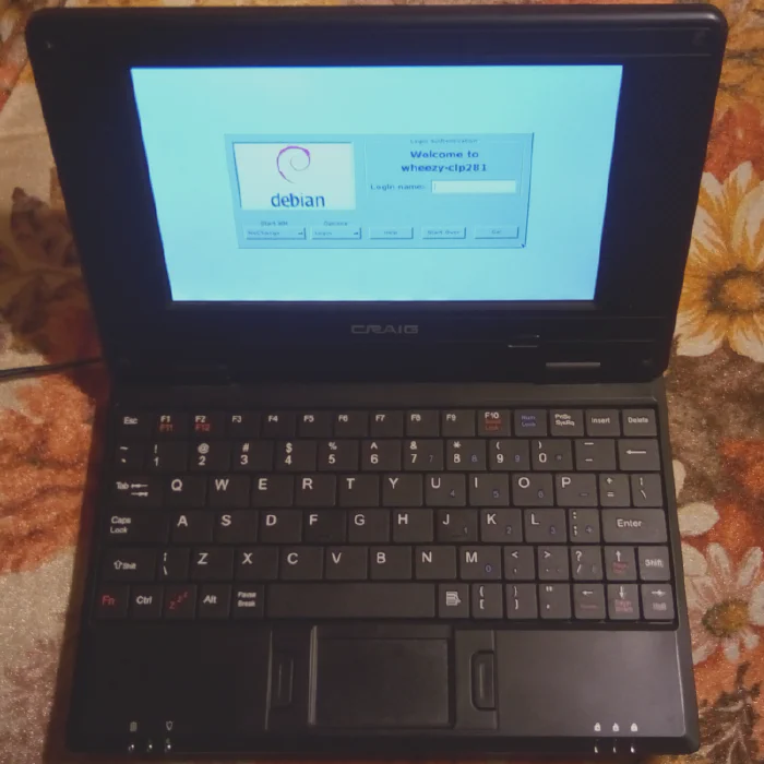 Top view of a black Craig CLP281 netbook showing the keyboard, touchpad, and a login screen for Debian Linux