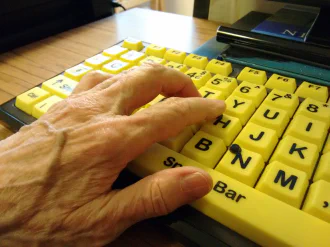 A hand with varicose veins rests on an a high contrast accessible computer keybard