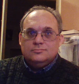 A cleanshaven middle-aged man wearing glasses and a dark green sweater