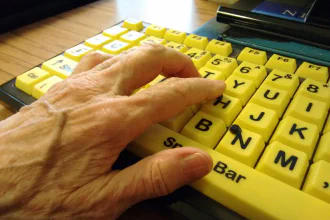 A hand with varicose veins rests on an a high contrast accessible computer keybard